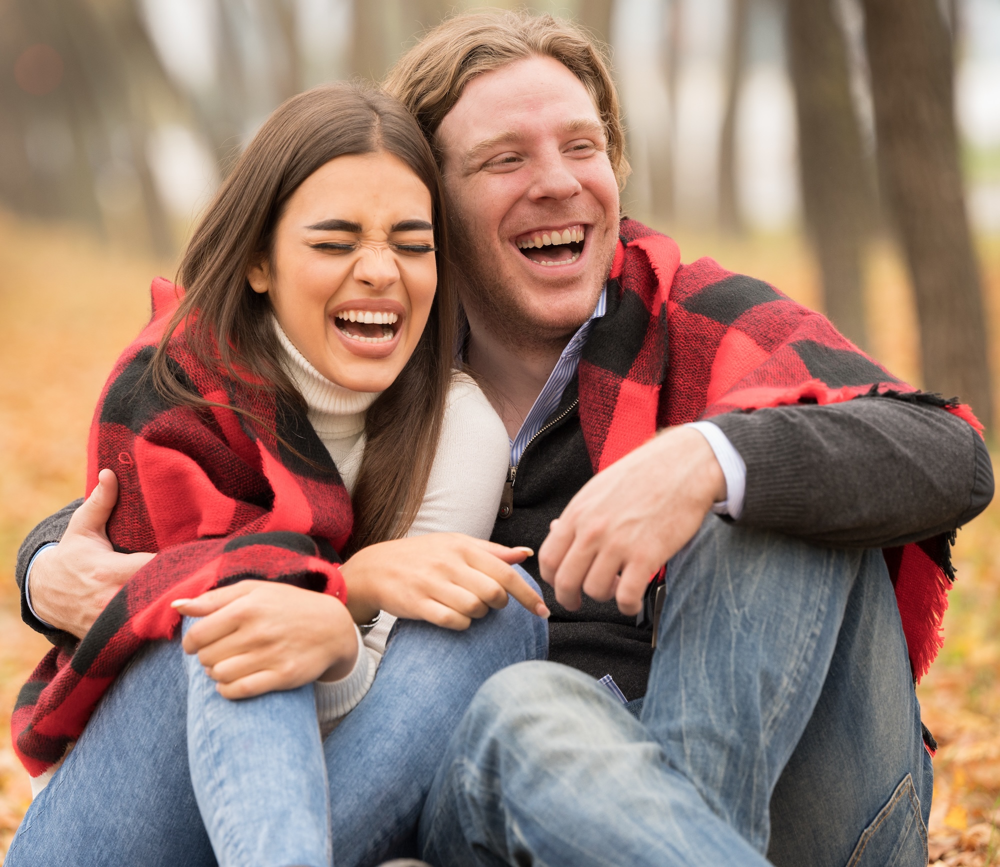 A loving Caucasian couple hugging  with a blanket on them sitting in the fall forest